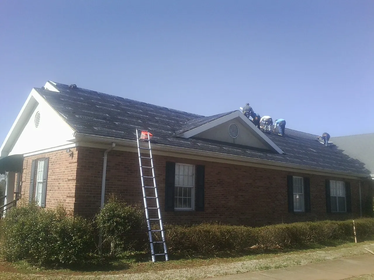 Crew tearing shingles off a brick ranch roof with a ladder set — Emergency Roof Repair work by our crew in Carteret