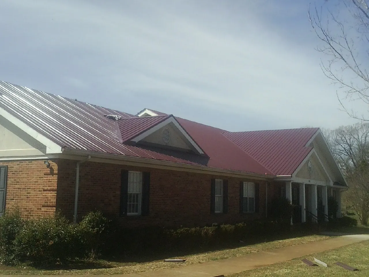 Red metal roof with gabled entries on a long brick building, from a Hail Damage Roof Repair job in Carteret