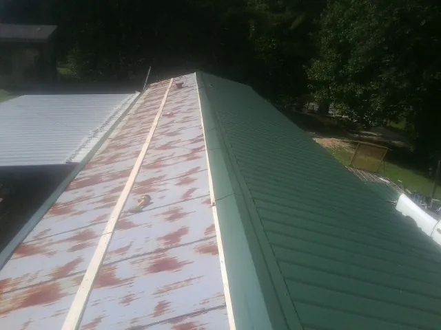 Old rusted panels beside newly installed green metal roofing — Wind Damage Roof Repair by Roofing Brothers in Carteret