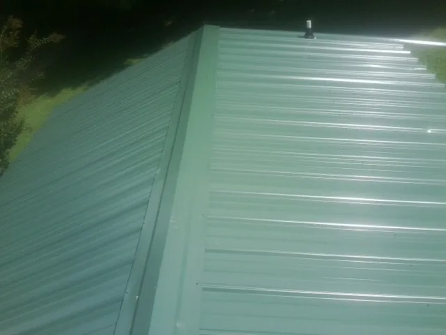 New green metal panels meeting at the ridge of a roof — Flat Roof Repair work by our crew in Carteret