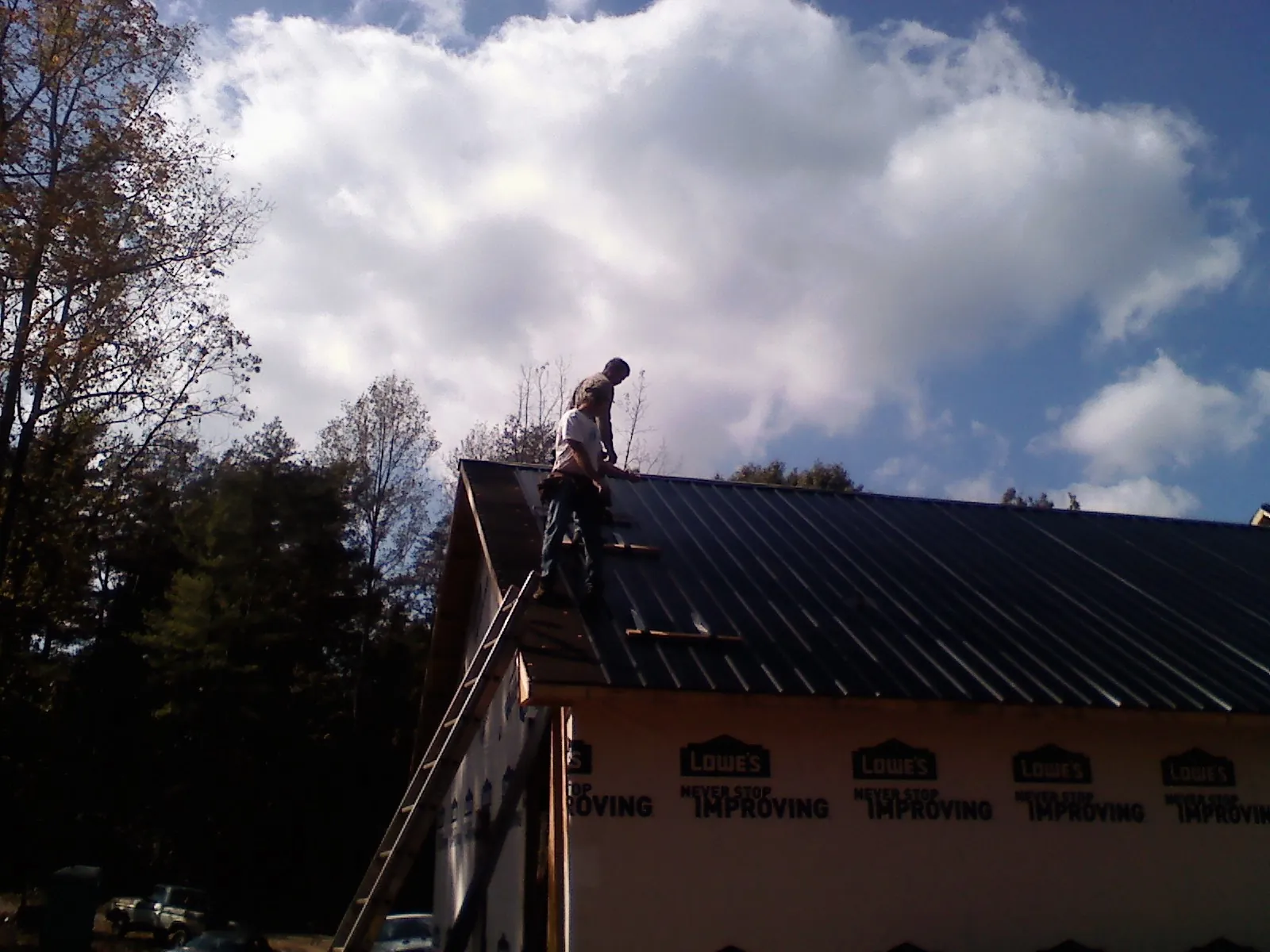 Roofer fastening dark metal panels high against a cloudy sky, from a Roof Inspection job in Carteret