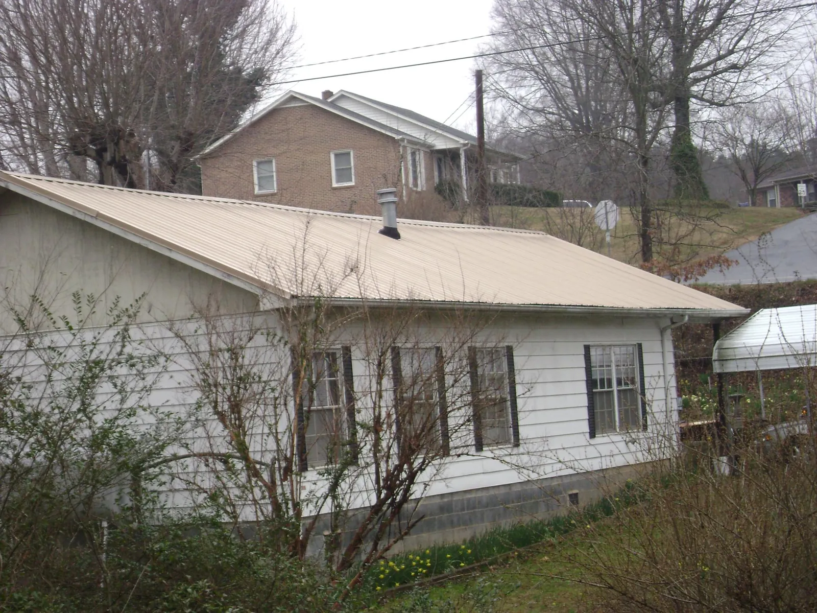 Tan metal roof on a white sided house set into a hillside — Commercial Roofing by Roofing Brothers in Carteret
