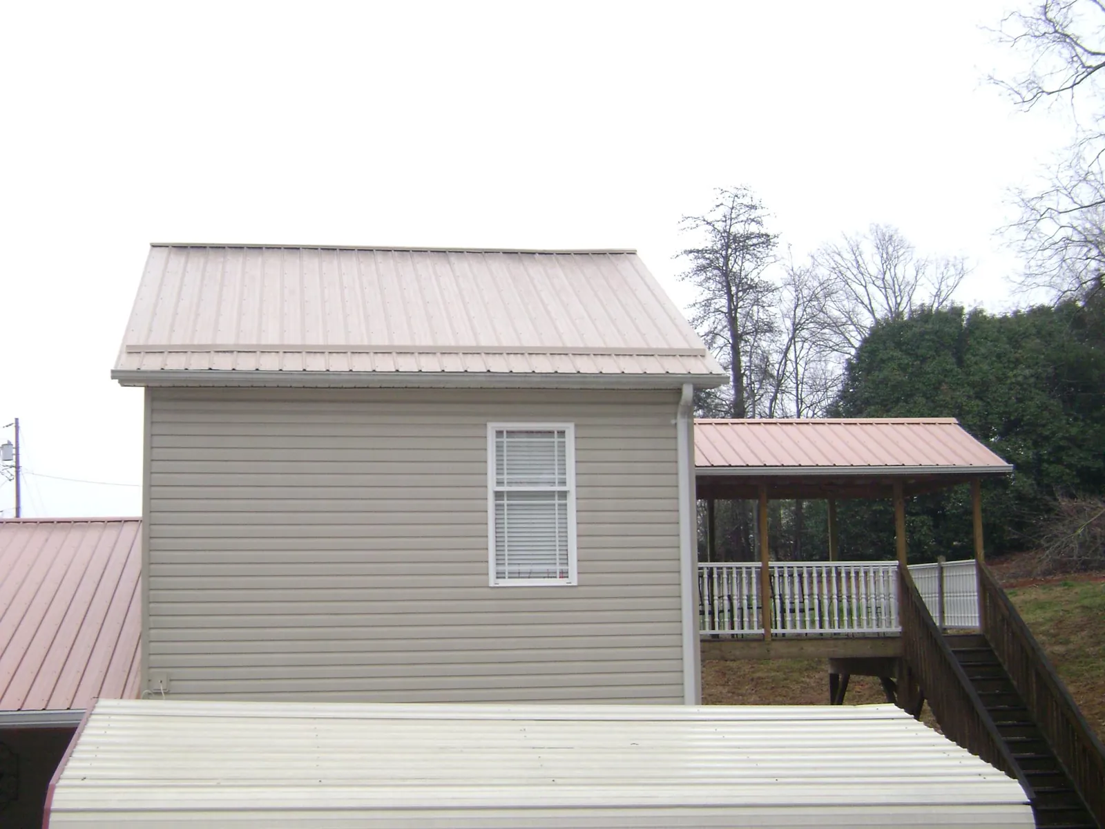 Tan metal roofs on a two story addition and attached porch, from a Roof Replacement job in Carteret